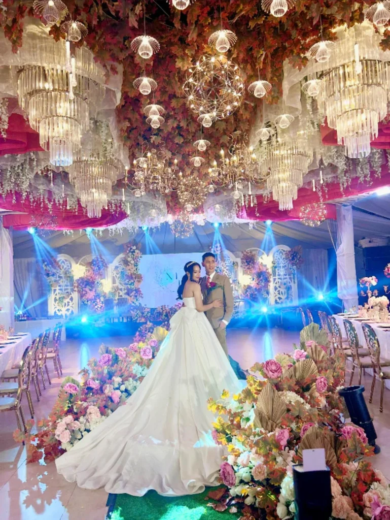 Bride and groom standing on an elegantly decorated wedding stage with floral and chandelier lighting