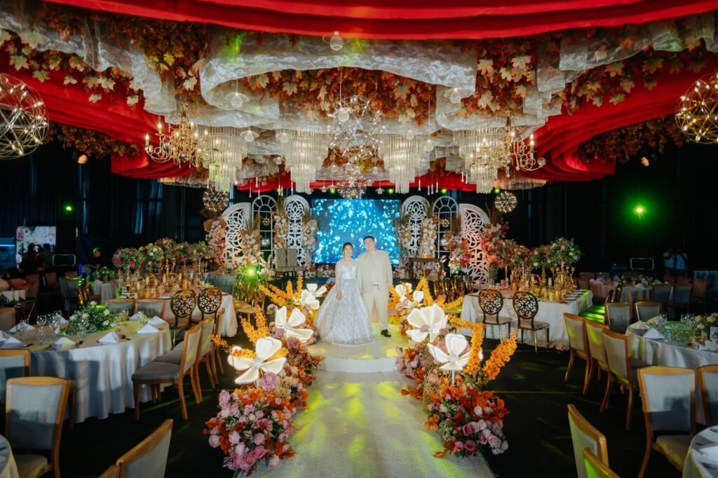 Bride and groom standing on an elegantly decorated wedding stage with floral and chandelier lighting.
